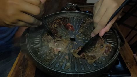 handheld close-up of two people using chop sticks while cooking beef