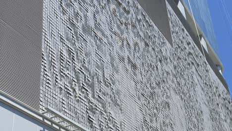 a textured surface resembling waves or ripples, part of a building situated in brickell, miami, glimmers under a clear, sunny sky, adding a modern architectural touch to the vibrant area.