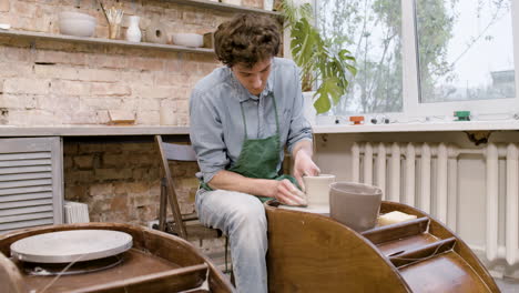 empleado en delantal verde modelando pieza de cerámica en una rueda de alfarero en un taller