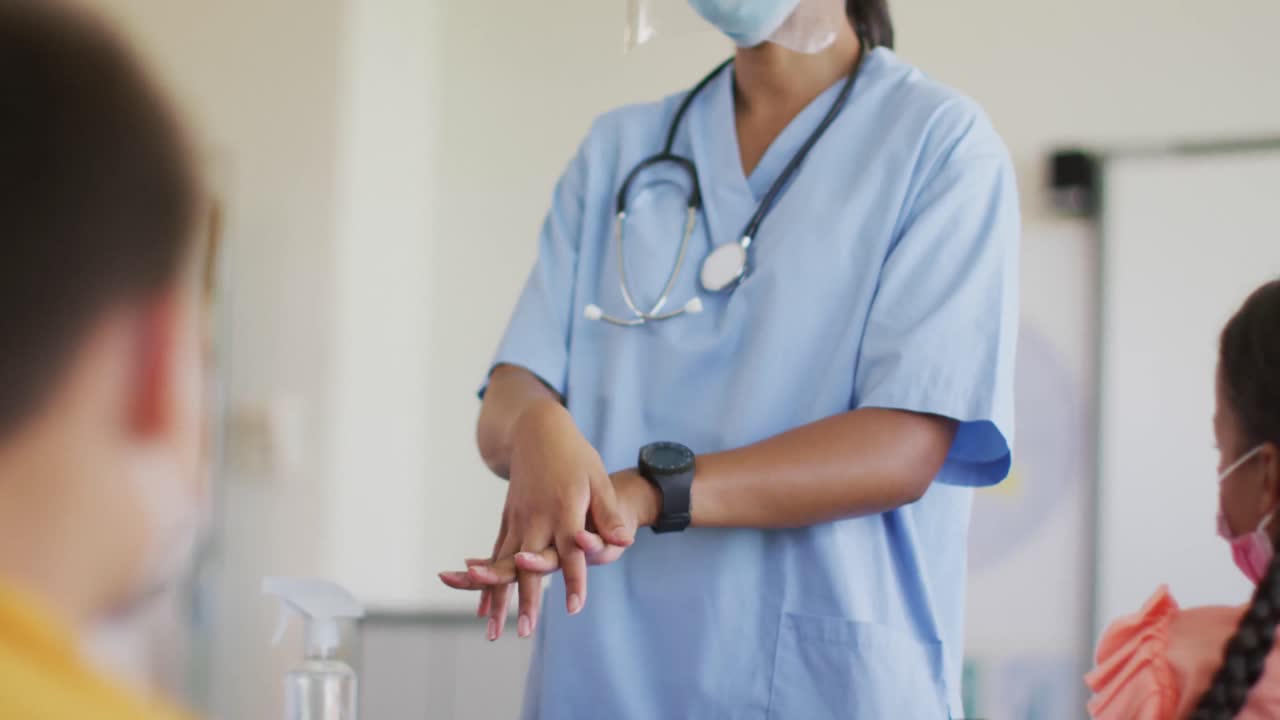 trabajadora médica de raza mixta con máscara facial mostrando a los escolares cómo desinfectar las manos