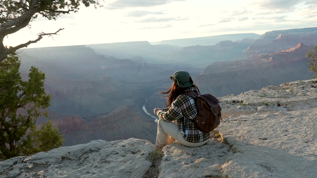 Donna con Zaino Seduta sul Bordo di una Scogliera Che si Affaccia sul Grand Canyon