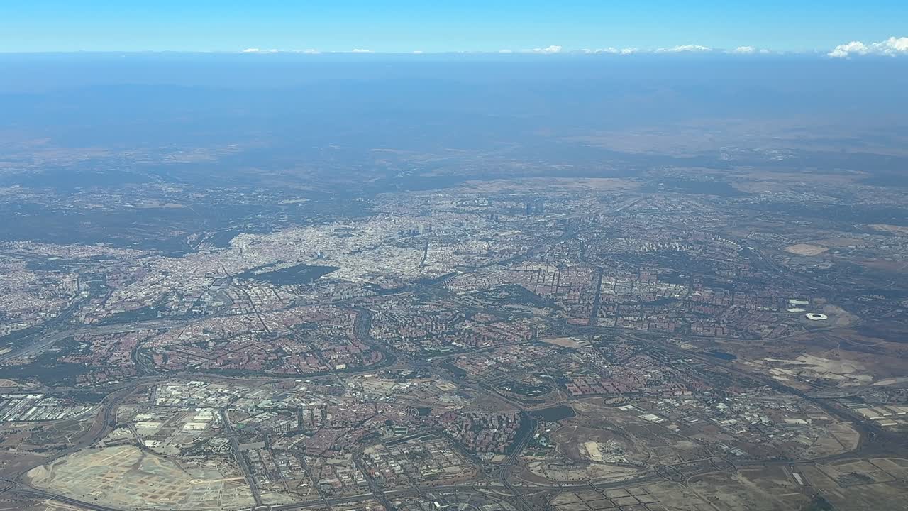 An elevated aerial view taken from a plane cockpit of Madrid city in a hazy summer morning under a splendid blue sky