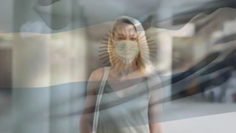 Animation-of-flag-of-argentina-waving-over-caucasian-woman-wearing-face-mask-in-city-street