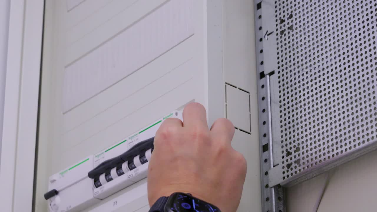 Close-up of a hand opening a fuse box and switching a breaker on inside an electrical panel
