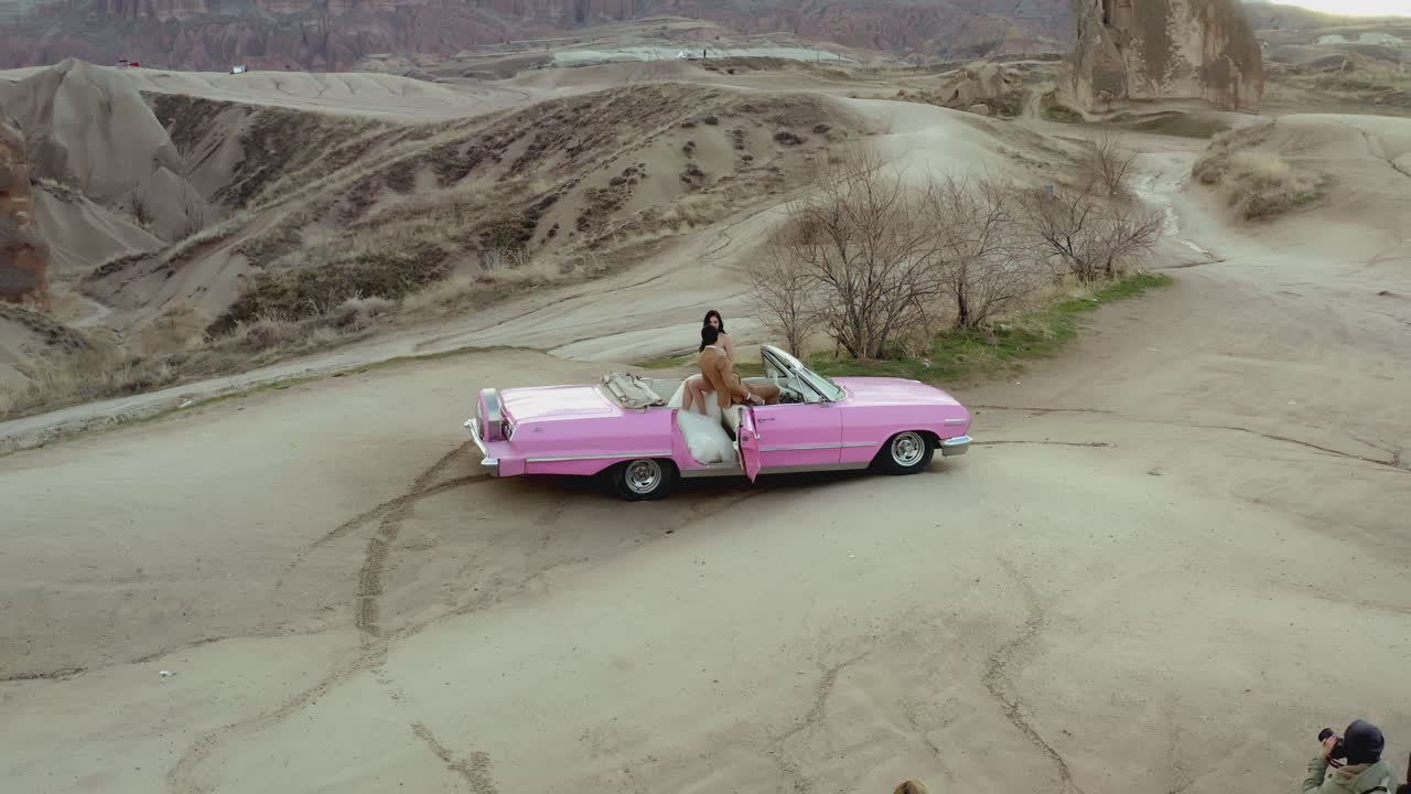 카파도키아 랜드스케이프의 빈티지 분홍색 컨버터블 자동차에 있는 부부