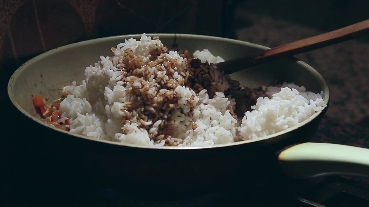 Drizzling soy sauce on a pan of rice and veggies to make fried rice recipe showing healthy home cooking and slow living