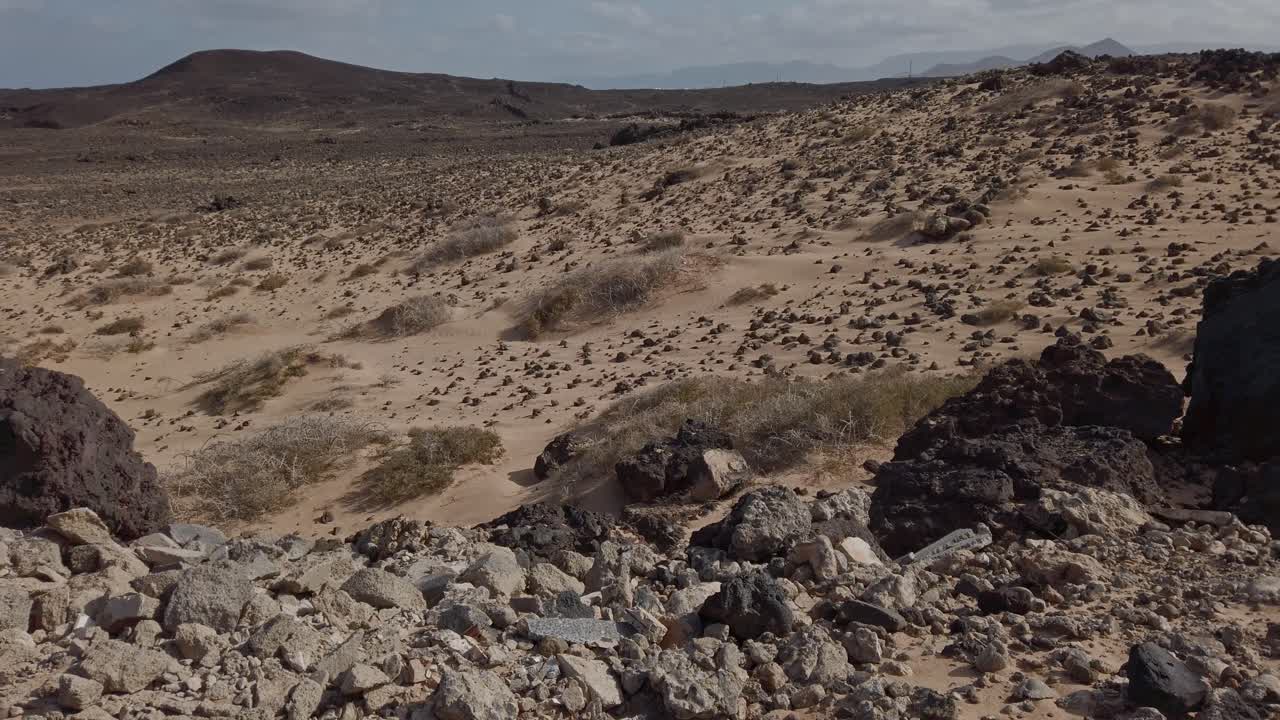 Volcanic landscape panning reveals a vast expanse of rocks and sand, gradually showcasing the distant ocean and a clear blue sky in lanzarote, canary islands
