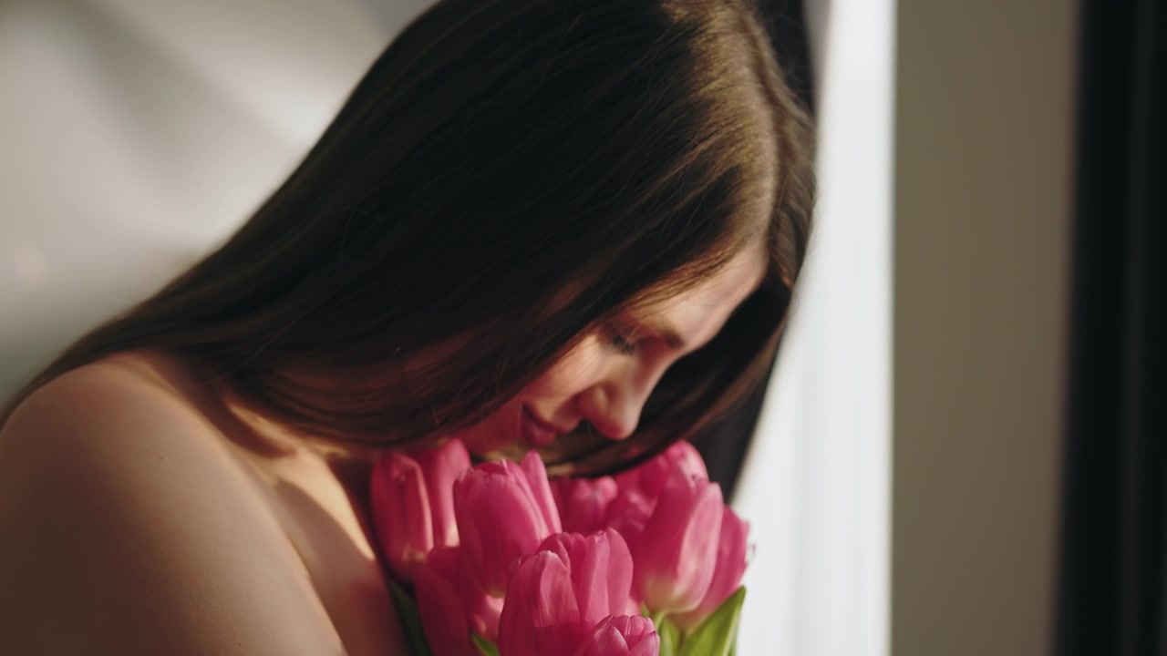 Ung kvinne lukter forsiktig på en bukett med rosa tulipaner