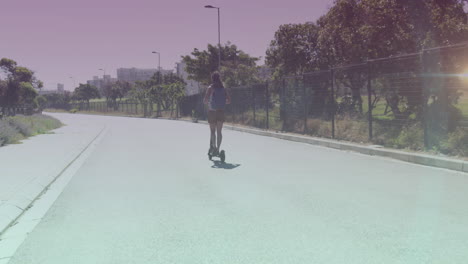 manchas de luz contra la vista trasera de una mujer afroamericana montando un scooter eléctrico en la calle