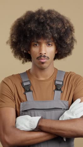 man with afro and mustache in overalls and gloves with crossed arms