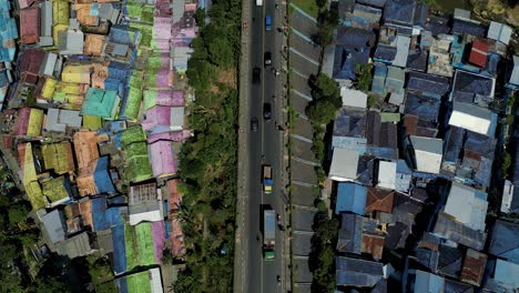 Vista-De-Pájaro-Mirando-Hacia-Una-Carretera-Con-Autos-Pasando-Por-Ella-Y-Rodeada-Por-El-Colorido-Pueblo-De-Jodipan-Y-La-Ciudad-Azul---Malang,-Java-Oriental---Indonesia