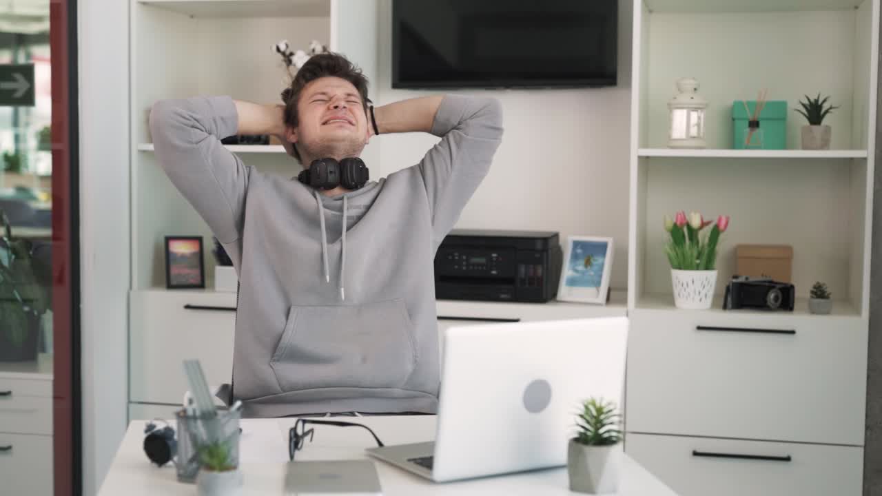 The charismatic young man sits at the table, attentively looking at the laptop screen, takes off his glasses, and becomes disappointed in what he sees. He appears slightly saddened.