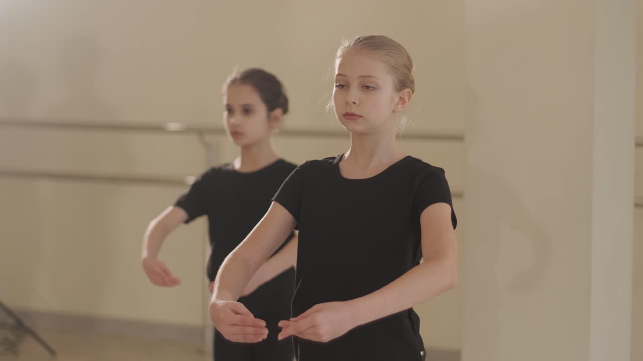 группа молодых студентов балета в черной танцевальной одежде практикует позиции в просторной балетной студии с деревянным полом и настенными решетками. сосредоточенные выражения и синхронизированные движения.