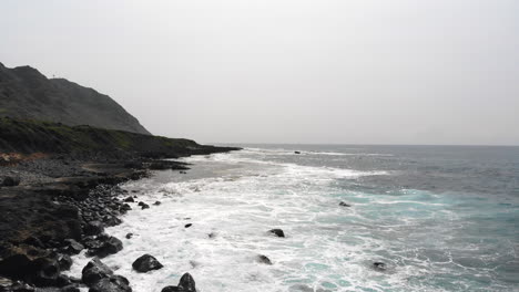 Imágenes-Aéreas-De-Hermosas-Olas-Del-Océano-Rompiendo-En-La-Costa-De-Hawaii-Con-Montañas-En-El-Fondo