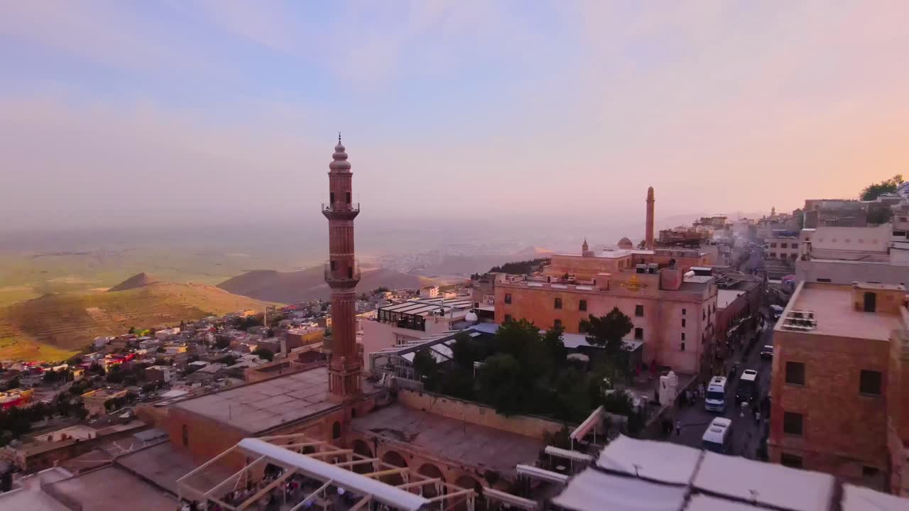 Vista panoramica con drone della città collinare di Mardin, Turchia, al tramonto, con doppi minareti che si innalzano sopra edifici in pietra, luce calda sul paesaggio, una vista scenografica di viaggio e patrimonio culturale.
