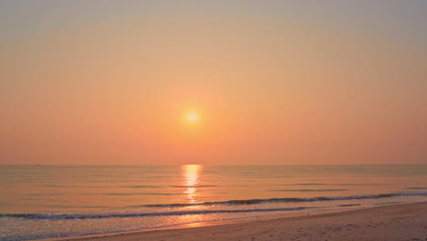 Amazing-golden-seaside-sunset-waves-slowly-rolling-towards-the-sandy-beach-in-Bali,-camera-pans-left