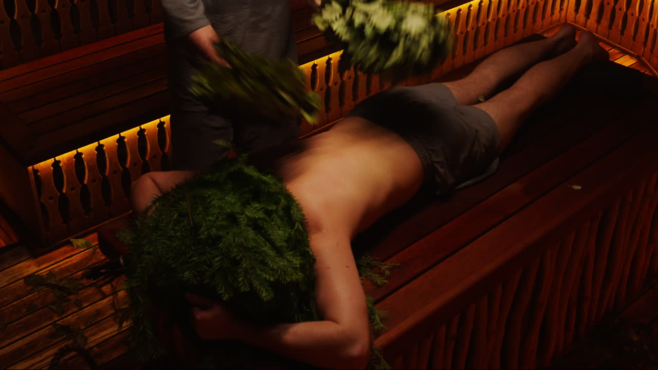 Man receiving sauna treatment with fir branches