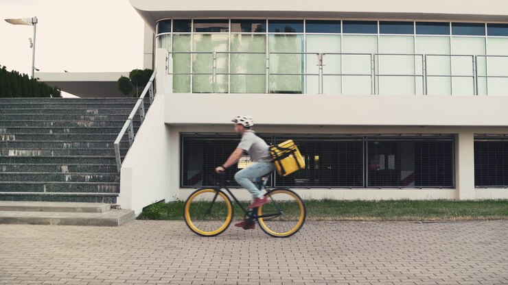 Ein Essenslieferant mit Thermorucksack stellt sein Fahrrad ab und geht die Treppe hinauf, um eine Lieferung abzugeben