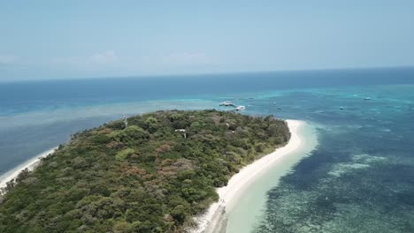 Die-Drohnenantenne-Bewegt-Sich-Nach-Unten-Und-Schwenkt-Nach-Links,-Um-Eine-Kleine-Tropische-Insel-Auf-Einer-Blauen,-Klaren-Insel-Zu-Zeigen