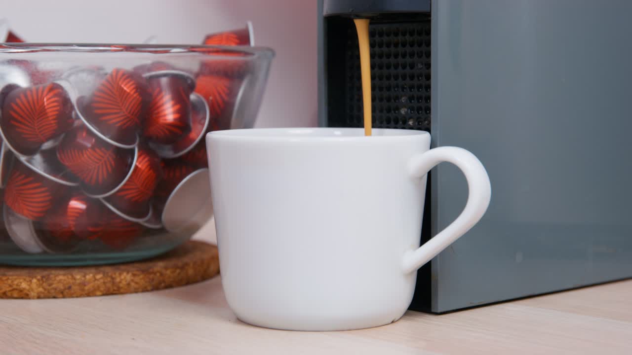 Man takes cup of coffee made by coffee machine standing on wooden table. Male person enjoys hot drink in kitchen in early morning close view