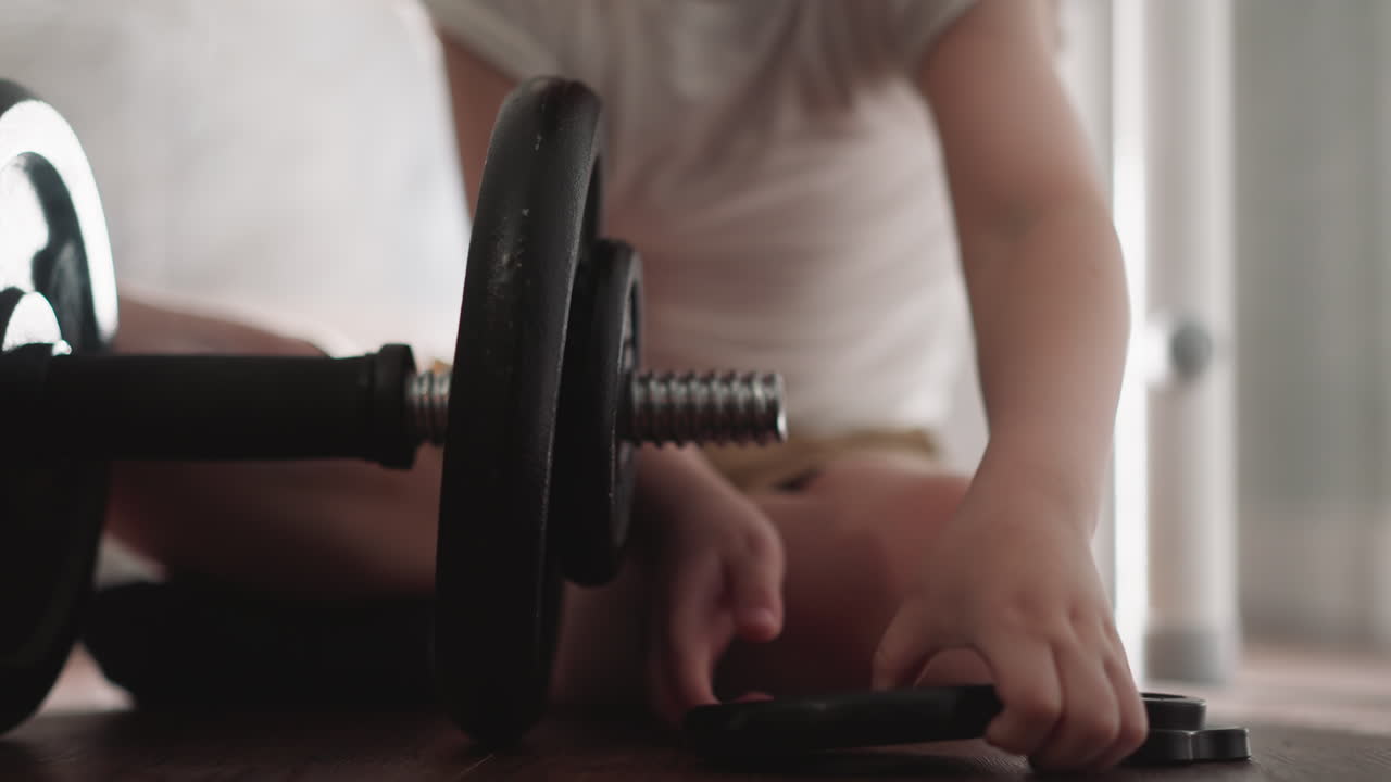 작은 소년은 운동을 위해 무거운 바벨에 검은 반지를 넣습니다.