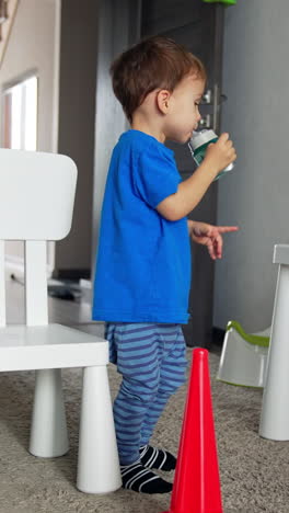 lovely toddler boy drinking water from a bottle. little kid sits down carefully on the white chair. vertical video