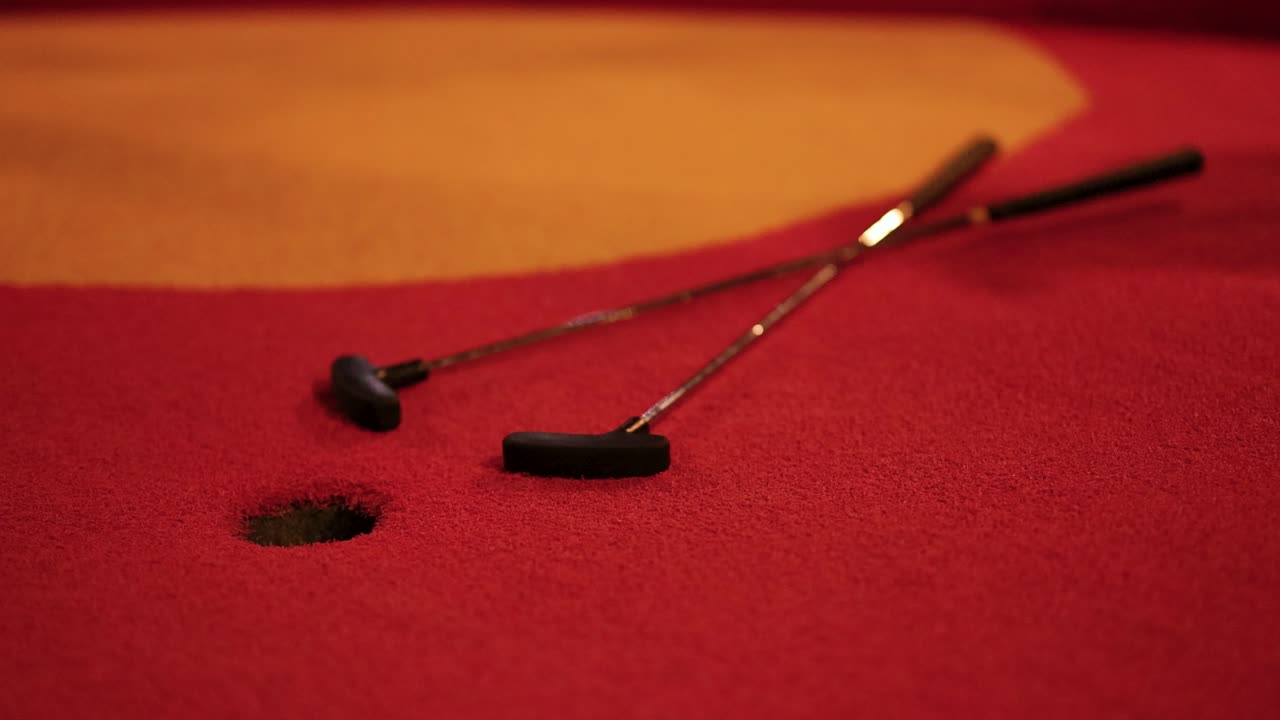 A red golf ball narrowly misses the hole on a vibrant red miniature golf course under warm lighting