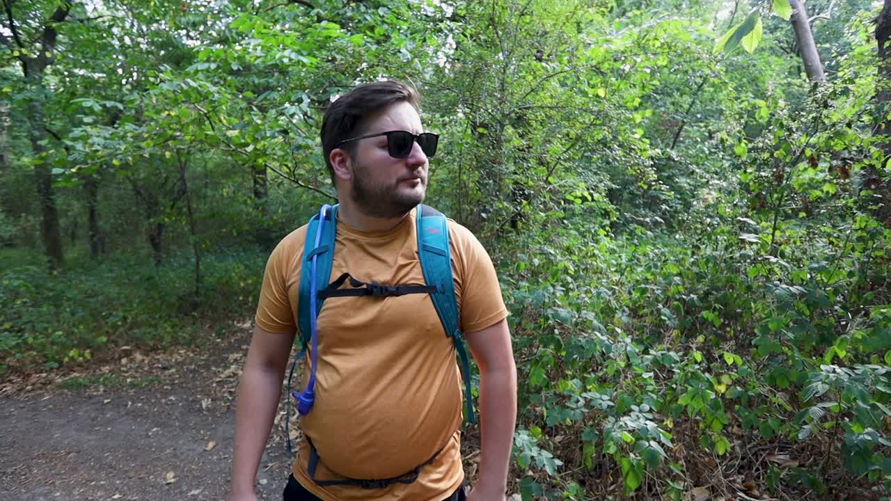 joven con mochila y gafas de sol se da cuenta de que está perdido en el bosque y camina hacia el otro lado