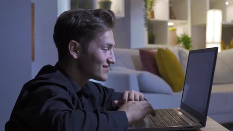 Joyful-man-working-on-laptop-at-home,-looking.