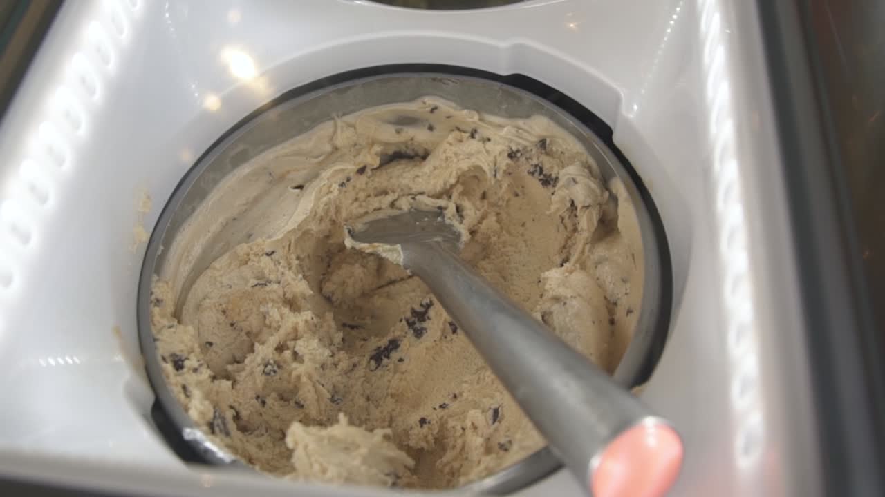 Gelato al caffè con gocce di cioccolato in vetrina con paletta, in mano