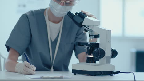 científica que utiliza el microscopio y toma notas durante las pruebas de laboratorio
