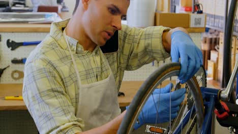 Man-talking-on-mobile-phone-while-repairing-bicycle-4k