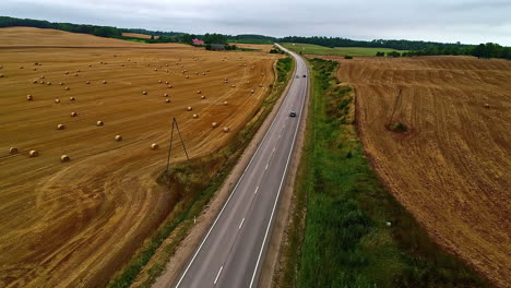 Coches-Conduciendo-Por-Una-Carretera-A-Través-De-Campos-Agrícolas-Con-Pacas-De-Heno-Recién-Cortadas---Vista-Aérea