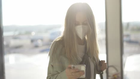 Mujer-Enmascarada-Usando-Un-Teléfono-Celular-Personal-Para-Charlar-Con-Amigos-En-Línea-Mientras-Espera-El-Vuelo