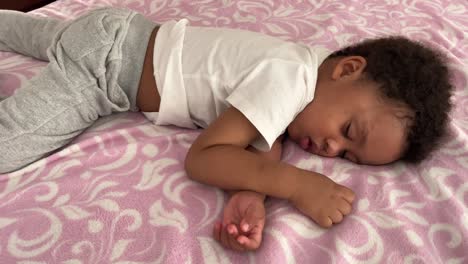 encantador y exótico niño de dos años de raza mixta durmiendo profundamente en su cama