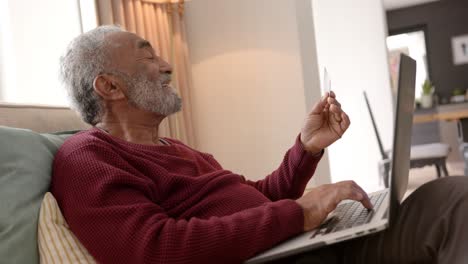 hombre biracial senior feliz usando una computadora portátil para comprar en línea, inalterado, en cámara lenta