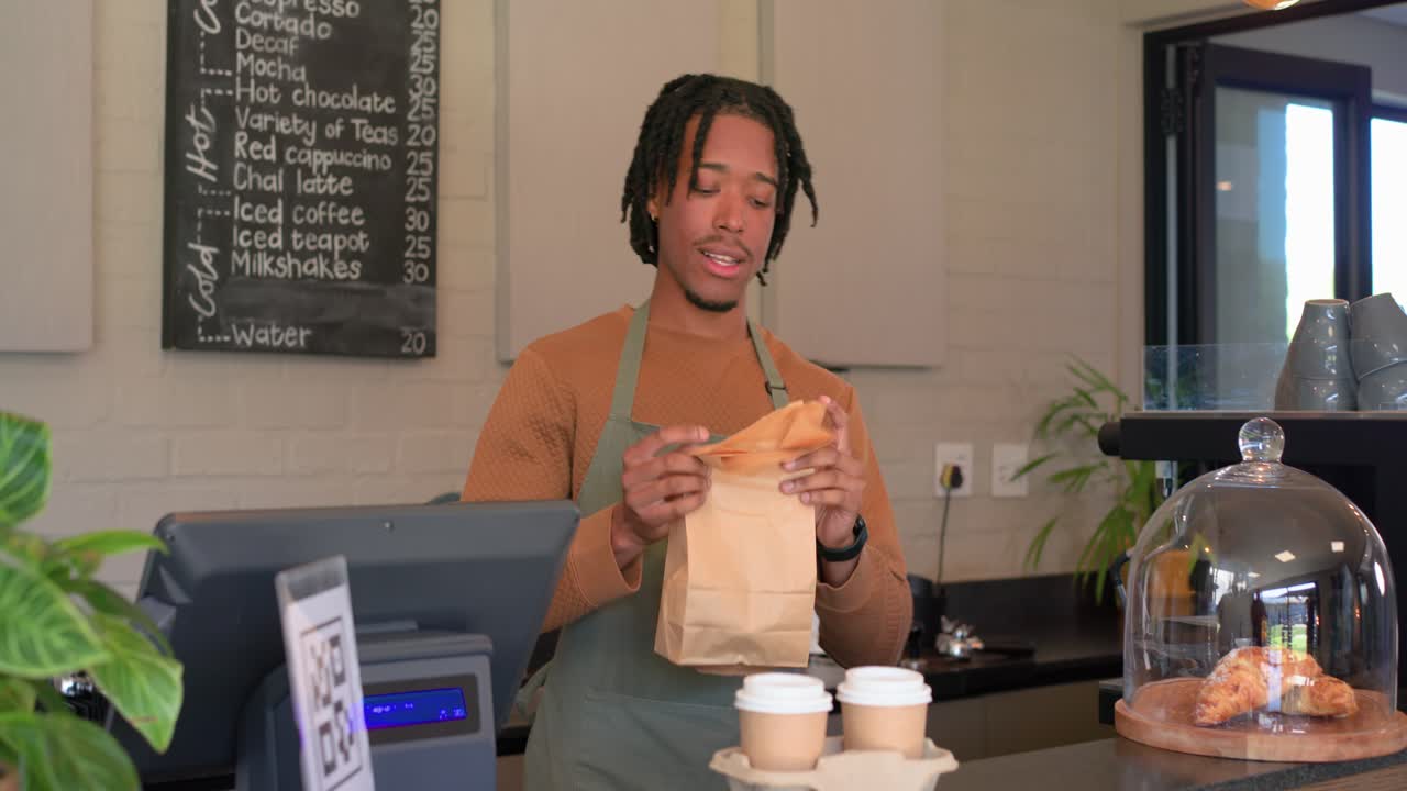 Picking up bag, male barista packing two coffee cups at register counter completing transaction