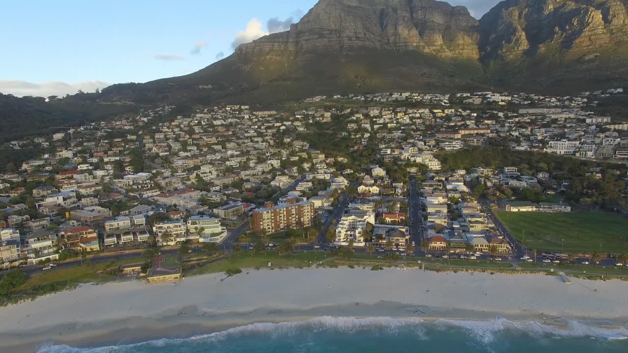 Aerial Shot of Waves hitting the beach in Camps Bay during Sunset with Table Mountain in the background