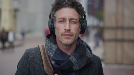 portrait attractive mature businessman wearing headphones listening to music enjoying relaxed urban commuting lifestyle on city street slow motion