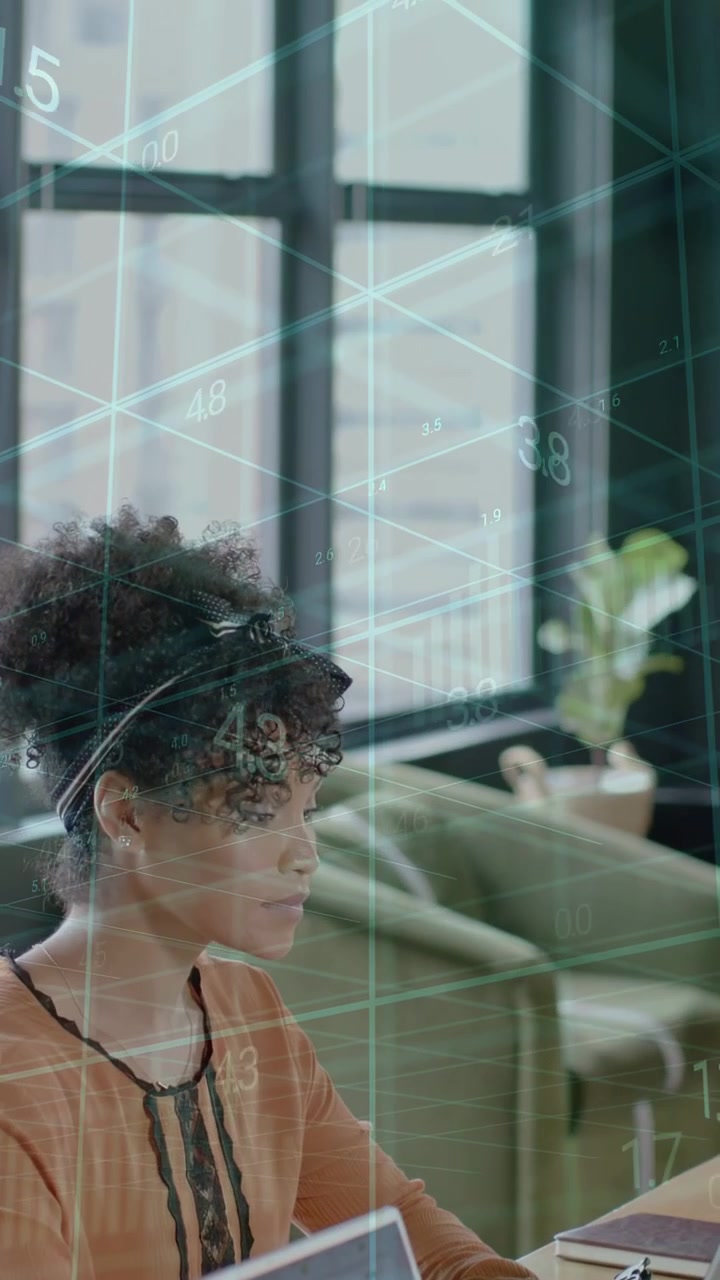Vertical video: Woman typing at desk, initiating tech overlay across workspace and analyzing chart