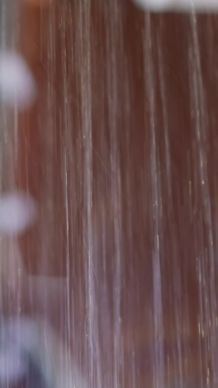 Young woman in black bikini takes shower washing back and arms under hot running water streams against blurred background slow motion closeup