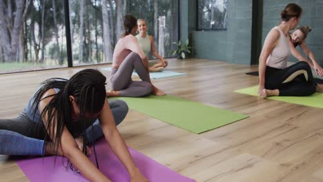 Focused-diverse-women-stretching-together-on-mats-in-yoga-class-with-female-coach,-slow-motion