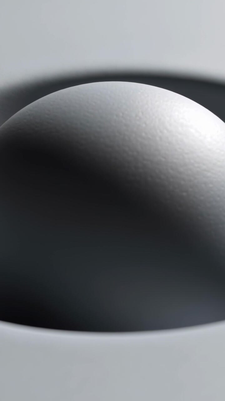 Vertical video: Pulling back, camera revealing matte gray sphere in dish, showing soft light study