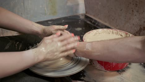 a potter teaches a woman to make clay dishes. a man takes a woman's hands