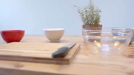 Close-up-of-bowls,-cutting-boards-and-knife-on-wooden-table-in-kitchen,-slow-motion