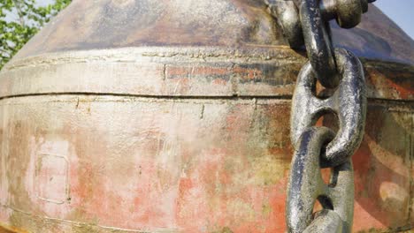 a heavy iron chain dangles from a weathered buoy embedded in the cement sidewalk