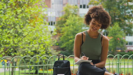 Mujer-Joven-Al-Aire-Libre-En-El-Parque-Sentada-En-Un-Banco-Trabajando-Escribiendo-En-Un-Cuaderno