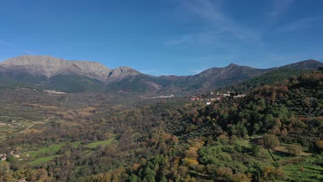 reverse flight with a drone in a valley in the fall season with diverse colors in the trees and the forest with a background of spectacular mountains on a sunny day with a blue sky