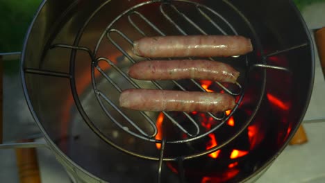 fresh sausages grilling on small barrel grill