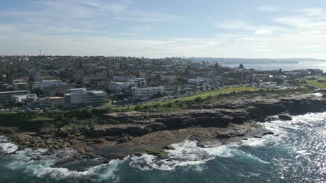 aerial fly over and zoom in at the beach side waterfront neighborhood homes and coastal residential properties with sydney city cbd skyline in the background